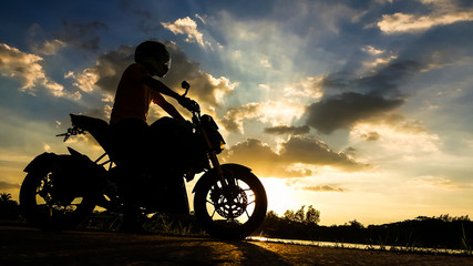 Obraz na płótnie Canvas Silhouette biker with his motorbike beside the natural lake and beautiful twilight sky.