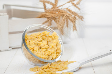 pasta in a transparent plate of glass and wooden spoon on a white old wooden boards