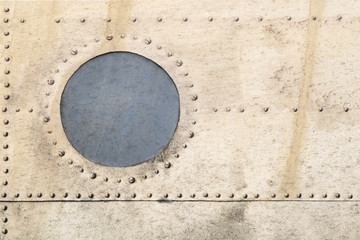 Old metal surface of the aircraft fuselage with round porthole
