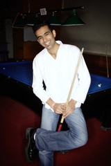 Young man leaning against pool table, holding pool cue