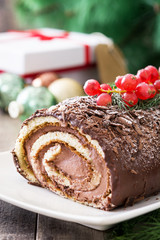 Chocolate yule log christmas cake with red currant on wooden background
