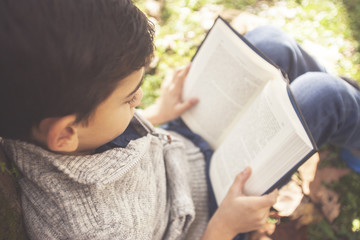 Little boy reading a book in the park. Learning and education concept