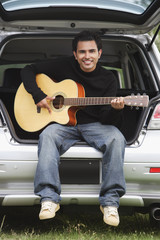Fototapeta na wymiar Young man sitting car boot playing guitar