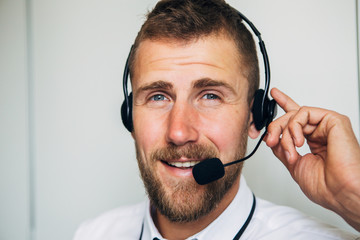 Portrait of handsome young male operator in headset looking at camera and smiling while standing against white background