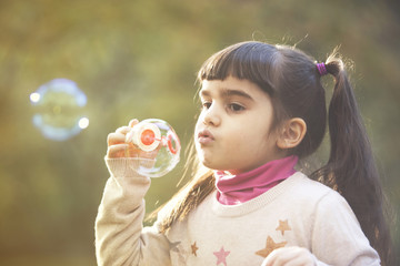 Cute little girl blowing soap bubbles in the park