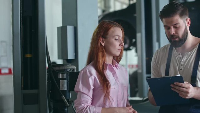 Tracking shot of female customer talking to mechanic at auto service center
