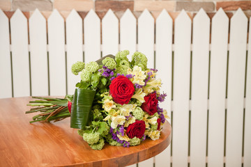 bouquet of flowers on a wooden round table against a white fence