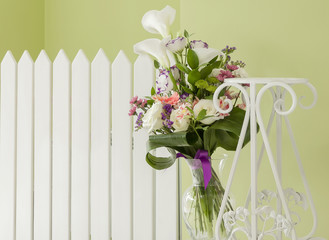 bouquet of flowers in a vase of glass against a white fence