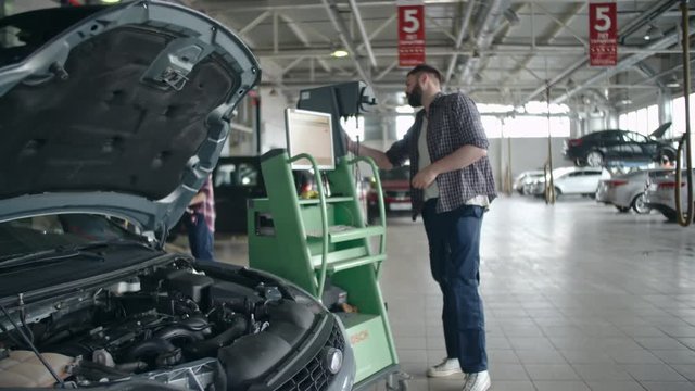 Car service worker using modern device connected with computer to do check-up of engine