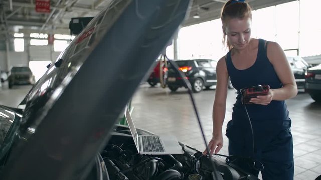 Woman using laptop to operate electronic device for car diagnostics in the repair garage