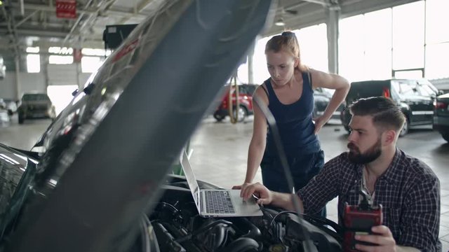 Two mechanics working with laptop to identify problem with car engine in auto service center