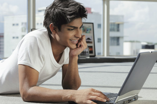 Profile Of Young Man Laying On His Stomach With Laptop