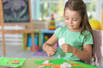 Llittle girl is cutting color paper