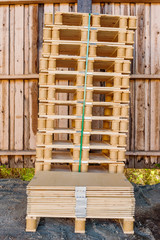 Stack of pallets and pallet material against wooden wall.