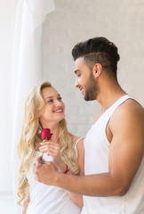 Young Beautiful Couple Stand Near Big Window, Hispanic Man Give Woman Red Rose, Happy Smile Lovers