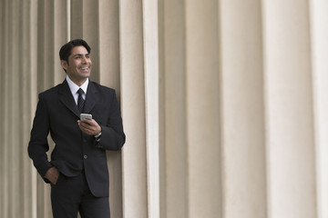 Businessman holding mobile phone, hand in pocket, smiling