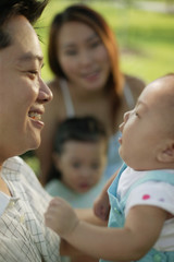 Father carrying baby, mother and young daughter in the background.