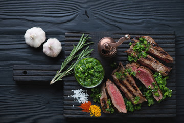 Grilled rump steak with chimichurri on a black wooden background