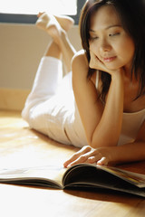 Young woman lying on floor reading magazine.