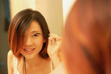 Woman putting on mascara, looking at mirror