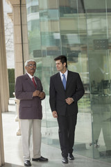 India, Senior and junior businessmen talking outside office building