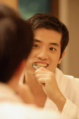 Young man brushing his teeth, looking in mirror