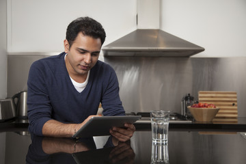 Singapore, Young man relaxing with tablet pc in kitchen