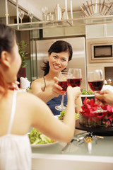 Friends toasting wine glasses across dinner table, over the shoulder view