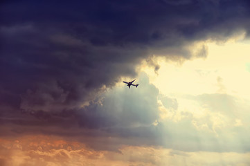 The airplane passenger jet fly right in to the dark clouds just before storm. Colorful sunset rays. Emergency concept.