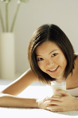 Young woman lying on front, holding glass of milk