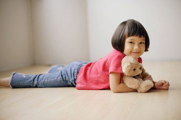 Young girl lying on front, hugging teddy bear.