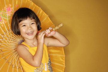 Young girl standing against yellow background, holding umbrella, laughing