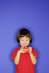 Young girl standing against blue background, holding an apple