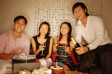 Couples sitting down, looking at camera, women holding wine glass