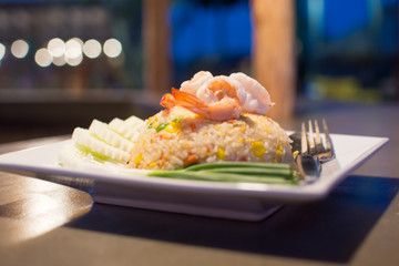 Shrimp fried rice dish is placed on a wooden table. Appetizing b