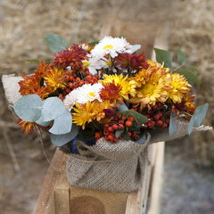 Autumn bouquet of yellow, orange, brown carnations with eucalyptus in a vase wrapped by canvas as decoration street market