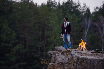 young handsome attractive bearded model man in forest with bonfire. Casual man, life style. Beautiful view on forest and rock