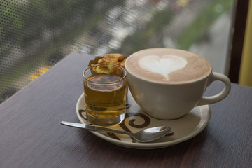 hot fresh coffee in white glass hot tea and alphabet biscuit with tree shape of heart foam on wooden table city view at sunset at coffee time / hot fresh coffee and tea