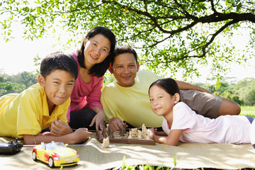 Family lying on mat in park, looking at camera