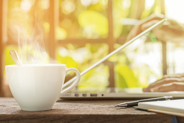 White hot coffee cup with businessman open laptop green garden background