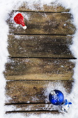 Weihnachtsmütze, blaue Weihnachtskugel und Weihnachtsglocke auf verschneiten Holzbrettern, Topview