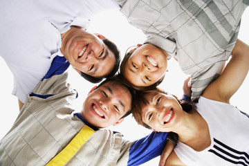 Fototapeta premium Family of four standing in a circle, arms around each other, looking down at camera