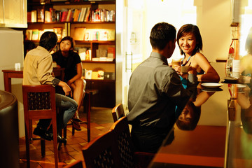 Couple at bar counter, sitting face to face, people in the background