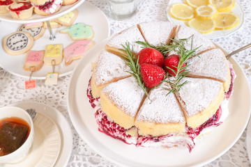 Classic Victoria sponge cake and other desserts served at the tea party, selective focus on the strawberries. Afternoon's high tea in Alice's mad tea party concept.