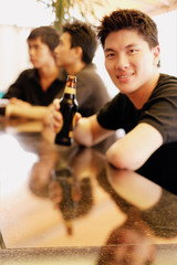 Young man at bar counter holding beer bottle, people in the background