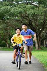Boy on bicycle, father running behind him, smiling