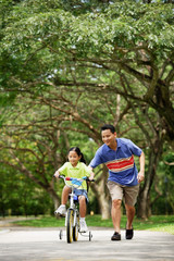 Girl cycling, father running alongside her