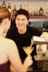 Man holding cocktail mixer, pouring drink for woman