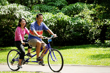 Obraz premium Couple riding tandem bicycle in park