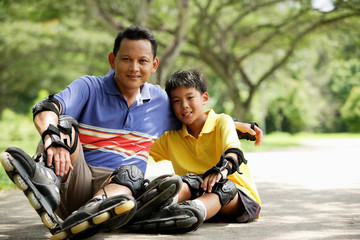 Father and son, sitting in park, wearing roller blades